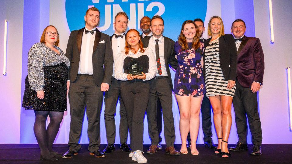 A group of staff from Loughborough stood on the stage holding an award and smiling at the camera